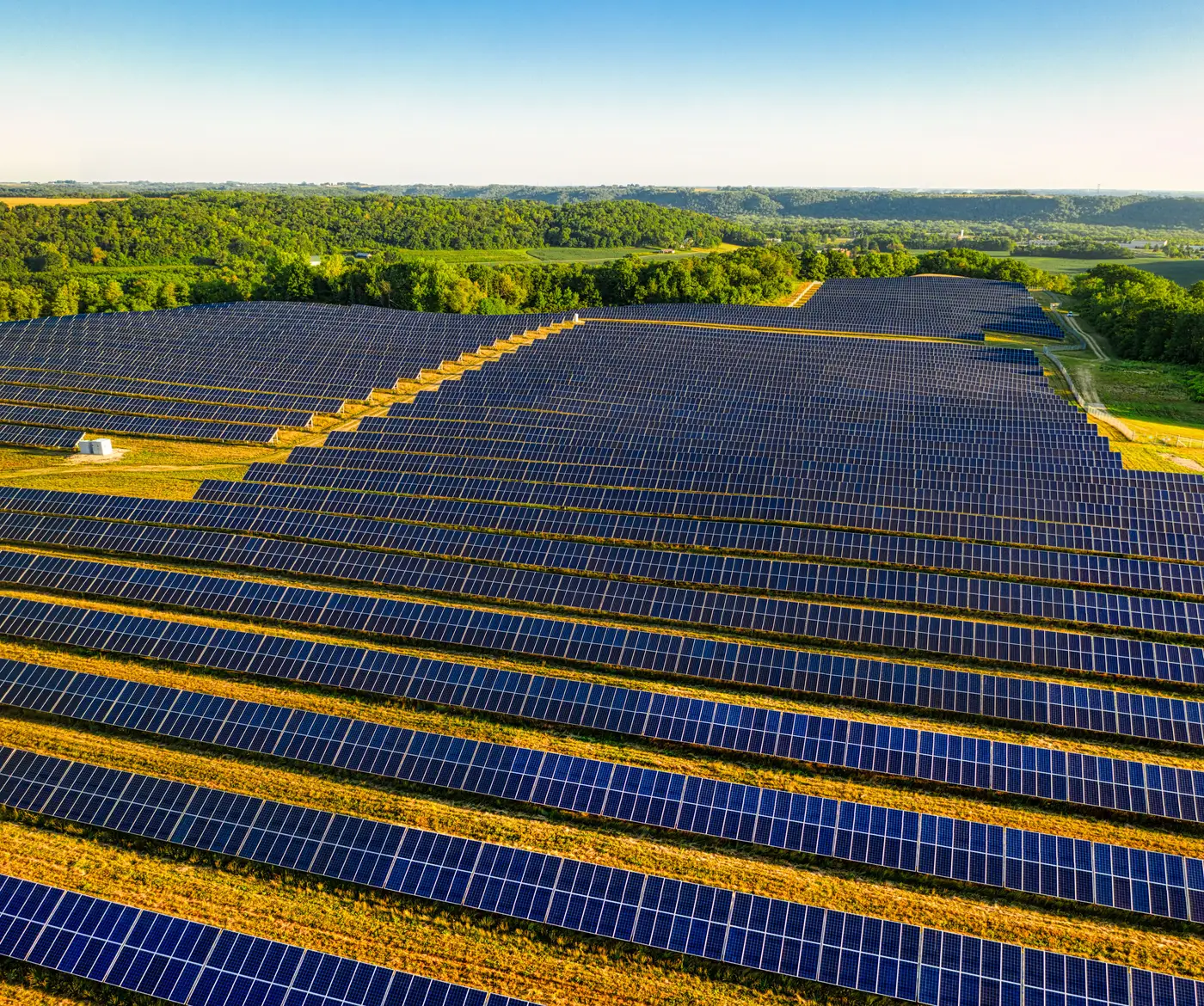 Aerial view of a large solar farm with thousands of panel rows covering rolling countryside